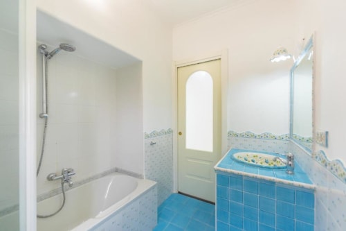 Bagno luminoso presso IL POETA a Procida con piastrelle azzurre, pareti bianche, vasca con doccia, lavabo, specchio e wc