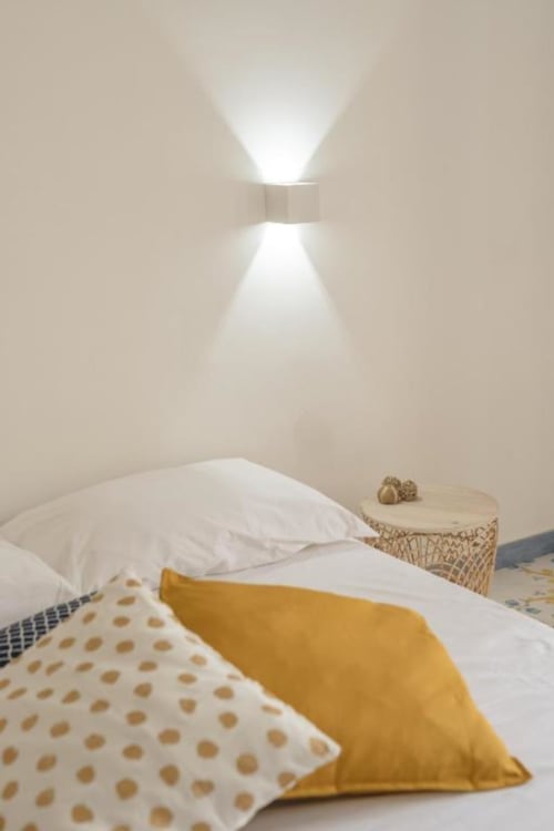 Camera moderna all'IL POETA a Procida con pareti bianche, arredamento minimalista, cuscino giallo e applique contemporaneo