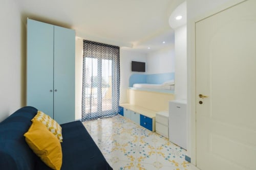 Camera luminosa nell'appartamento IL POETA a Procida con guardaroba blu, cuscino giallo, tappeto decorato e accesso alla terrazza