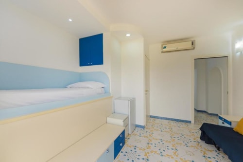 Camera luminosa con letti a castello blu e crema, climatizzatore e pavimento in cotto presso IL POETA, Procida