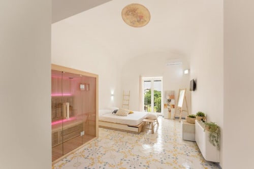 Suite moderna con sauna all'IL POETA B&B a Procida. Sauna con illuminazione rosa, letto bianco, porte sul terrazzo e pavimento in terrazzo.