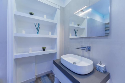 Bagno moderno nella suite IL POETA a Procida con lavabo bianco, specchio, scaffali e finiture contemporanee