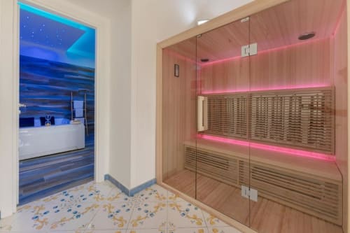 Moderna sauna con illuminazione LED rosa, porte in vetro e interni in legno presso IL POETA Suite a Procida