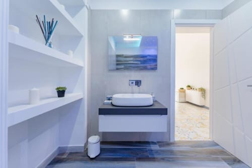 Elegante bagno di IL POETA, Procida con lavabo bianco ovale su mensola scura, opera d'arte marina blu e ripiani sospesi