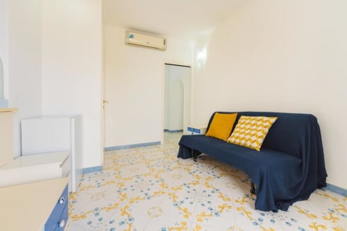 Camera da letto luminosa a Procida con divano scuro, cuscini gialli e pavimento piastrellato colorato vicino l'ingresso