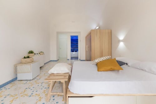 Luminosa suite moderna all'IL POETA di Procida con letti in legno, biancheria bianca, cuscino giallo e pavimenti in piastrelle decorate