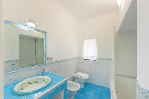 Bagno luminoso con piastrelle blu, lavabo, wc, bidet e specchio dell'appartamento IL POETA a Procida