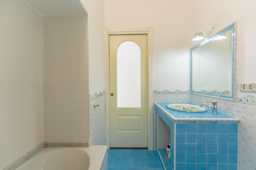 Bagno luminoso nell'appartamento IL POETA a Procida con vanity in piastrelle blu, vasca, specchio e dettagli decorativi.