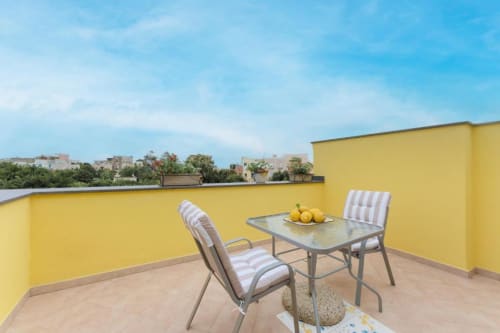 Terrazza soleggiata gialla a IL POETA a Procida con tavolo, sedie a righe e vista sulla città