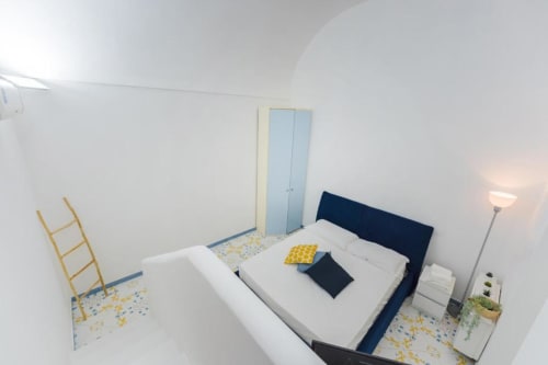 Camera luminosa nell'appartamento IL POETA a Procida con testata blu navy, biancheria bianca, dettagli gialli e guardaroba