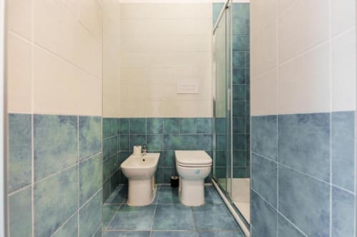 Bagno moderno a IL POETA Procida con piastrelle azzurro-verdi, WC, bidet, doccia e pareti superiori color crema