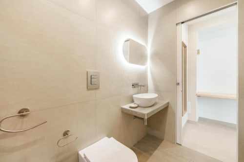 Bagno moderno di IL POETA a Procida con specchio illuminato rotondo, lavabo bianco a bacinella, wc e pareti con piastrelle neutre