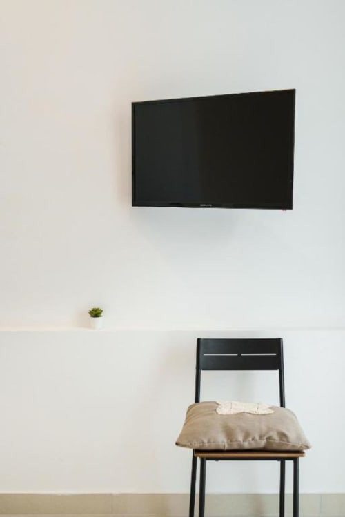 Camera minimalista all'IL POETA Procida con TV a schermo piatto a parete, pianta in vaso e sedia con cuscino