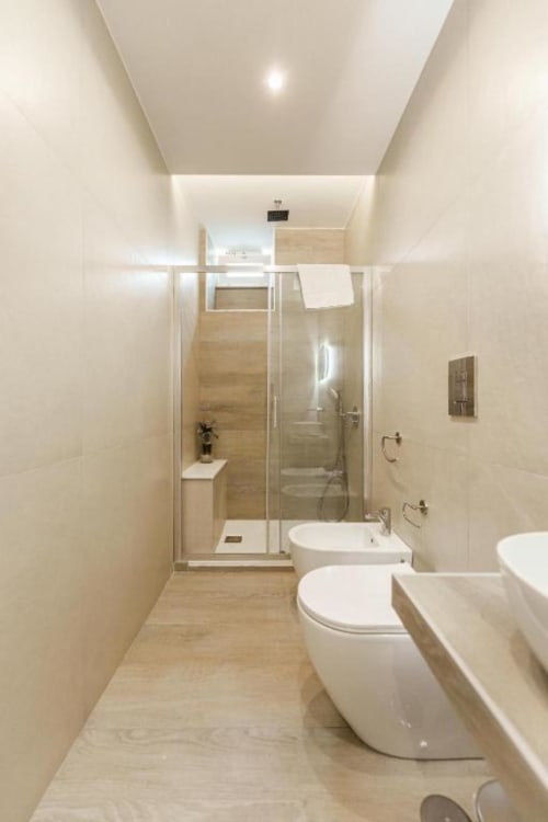 Bagno moderno in IL POETA Procida con toilette bianca, bidet, cabina doccia in vetro e finiture in tonalità legno