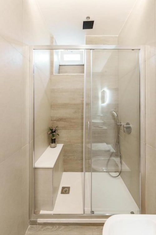 Doccia moderna con pareti in vetro, soffione pioggia, panca bianca e rivestimento in piastrelle beige nella Deluxe Room di IL POETA
