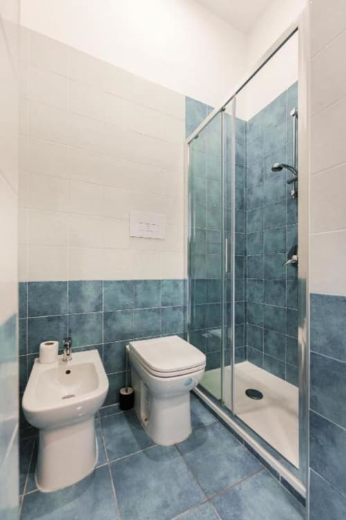 Bagno moderno in IL POETA Procida B&B con pareti rivestite di piastrelle blu, lavabo bianco, toilette e doccia con box in vetro