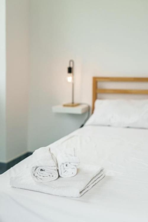 Asciugamani bianchi arrotolati e amenities sul letto della camera Il Poeta Procida con lampada da comodino e testata in legno