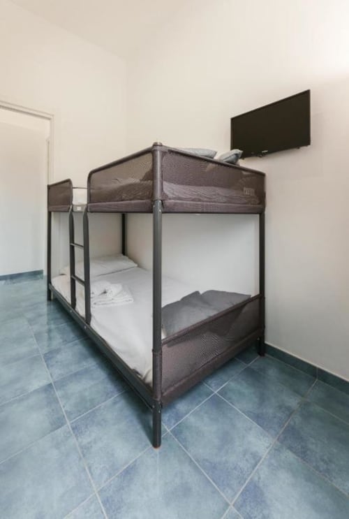 Letti a castello in camera quadrupla moderna di IL POETA, Procida. Letti con struttura metallica e materassi bianchi, TV a schermo piatto montata a