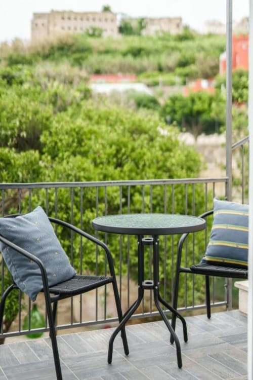 Area con sedute in balconata presso IL POETA a Procida con tavolo, sedie e vista lussureggiante sul paesaggio verde dell'isola