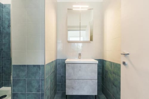 Bagno moderno di IL POETA a Procida con piastrelle turchesi, lavabo bianco, specchio contenitore e illuminazione luminosa