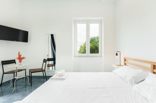 Luminosa Camera Quadrupla a IL POETA Procida con biancheria bianca, testata in legno, TV, zona pranzo e porte-finestre che si aprono su
