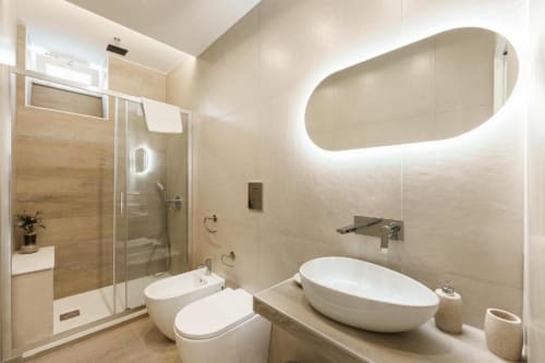 Bagno moderno in IL POETA Procida con lavabo bianco, wc, doccia walk-in e specchio ovale retroilluminato