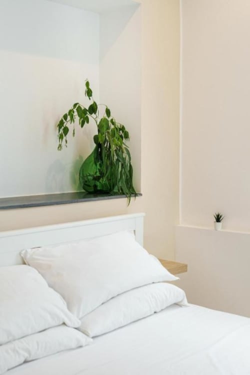 Camera da letto minimalista in IL POETA a Procida con biancheria bianca, cuscini e piante verdi in vaso su scaffale sospeso