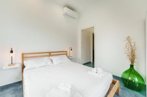 Camera moderna a IL POETA a Procida con letto in legno, biancheria bianca, vaso verde, aria condizionata e arredamento minimalista