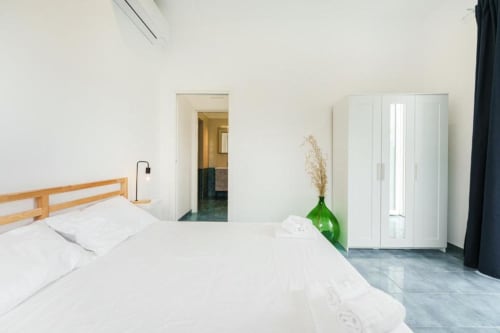 Camera luminosa e minimalista a IL POETA, Procida con letto in legno, armadio bianco e vaso verde su tonalità blu-grigio