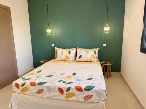 Chambre moderne de la villa Figari avec mur d'accent vert, linge de lit à motifs de feuilles, luminaires suspendus et tables de nuit en bois