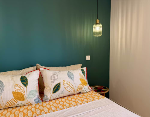 Chambre élégante avec mur d'accent bleu-vert, coussins à motifs de feuilles, lampe suspendue et linge blanc à la villa Figari