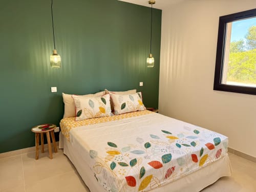 Chambre moderne dans une villa avec piscine privée à Figari, mur d'accent vert, linge de lit à motifs de feuilles, luminaires suspendus