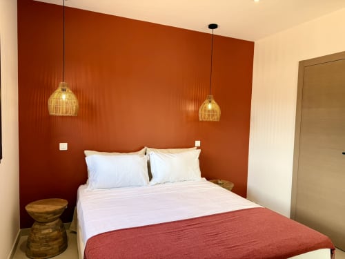 Chambre moderne avec mur d'accent rouille-orange, literie blanche, luminaires suspendus et table de nuit en bois à la villa Figari