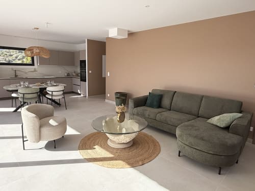 Salon moderne aux lignes ouvertes avec canapé gris, fauteuil crème, table basse ronde en verre et cuisine à Figari