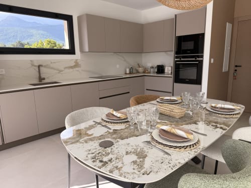Cuisine et salle à manger de villa moderne à Figari avec table en marbre, mobilier gris et vue sur les montagnes