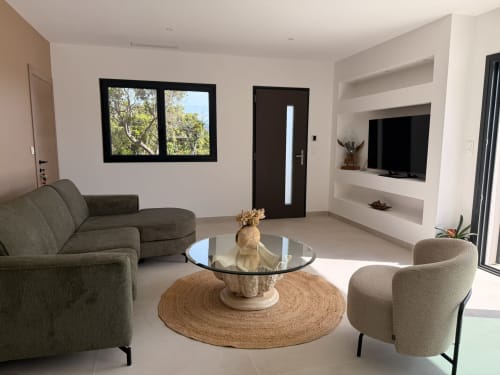 Salon moderne à Figari avec canapé gris, table basse ronde, TV écran plat et baies vitrées noires