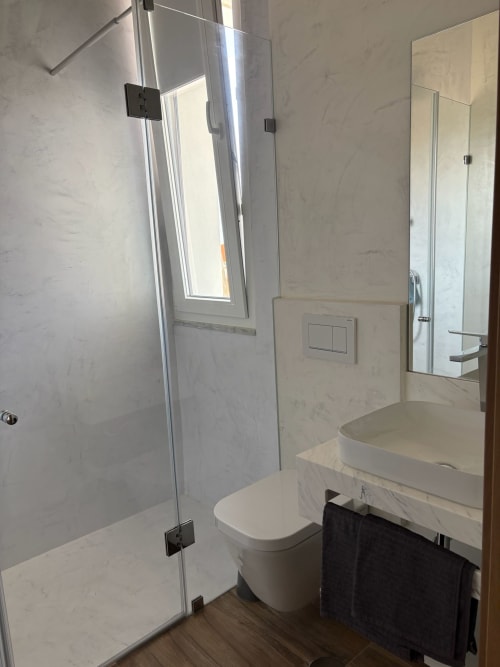 Modern bathroom in Torre T2 apartment at AL Patio Da Figueira hotel, Torres Vedras, with marble finishes, glass shower