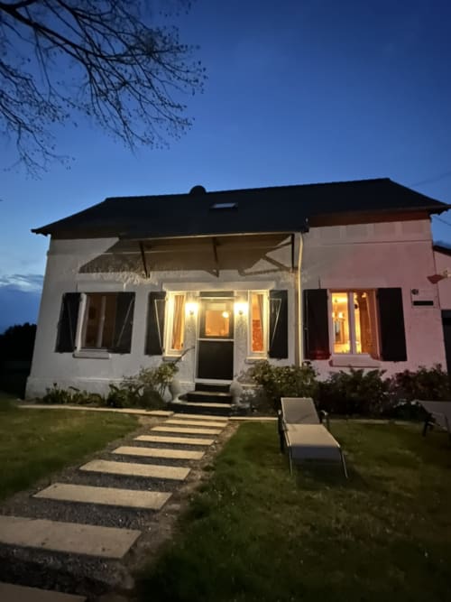Chaumière du Domaine de la Ferme de Ribeaufontaine illuminée au crépuscule, pelouse soignée et chaise longue de détente à Dorengt, France