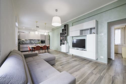Modern open-plan apartment in Verona with gray sofa, kitchen, dining area, and white TV unit against green walls