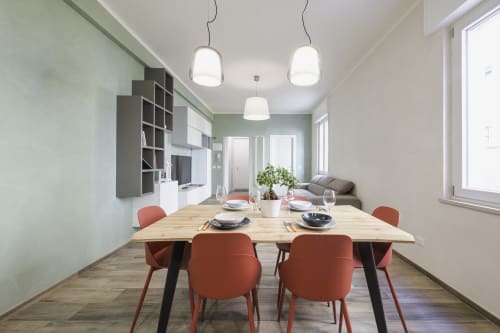 Modern dining area with wooden table, coral chairs, and pendant lights in Arena Gateway apartment, Verona