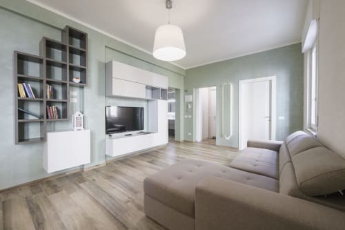 Modern living room in Verona apartment with gray sofa, TV, wooden floors, sage green walls, and built-in shelving