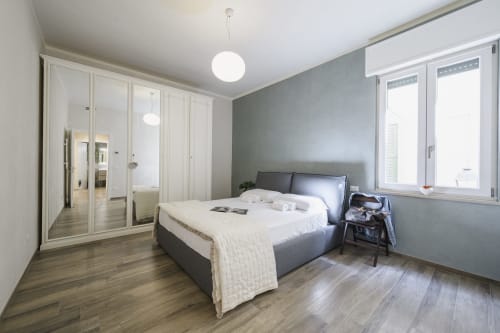 Modern bedroom at Arena Gateway apartment in Verona with gray bed, white wardrobe, wooden floors, and city views