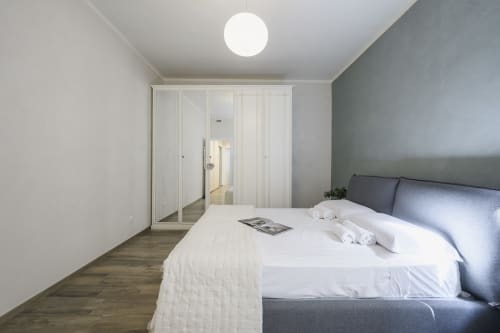 Modern bedroom at STAYIN VERONA with gray headboard, white bedding, mirrored wardrobe, and round ceiling light