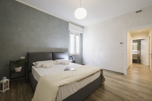 Modern bedroom in Arena Gateway apartment, Verona with queen bed, dark headboard, wooden flooring, and ensuite bathroom