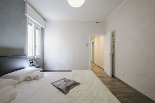 Modern bedroom at Arena Gateway apartment in Verona with bed, window, wooden floors, and open doorway