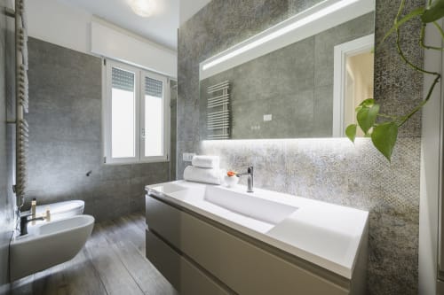 Modern bathroom in Verona apartment with gray tile walls, illuminated mirror, white sink, and toilet