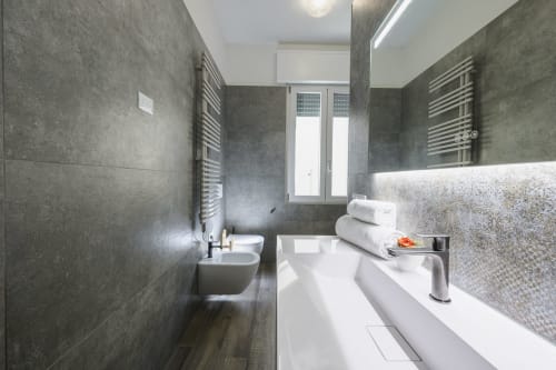 Modern bathroom with grey tile walls, white sink vanity, and heated towel racks in Arena Gateway apartment, Verona