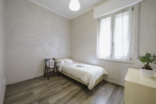 Modern bedroom in Verona apartment with single bed, wooden floor, large windows, and potted plant on desk