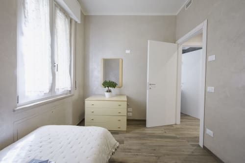 Bright modern bedroom in Verona apartment with double bed, yellow dresser, mirror, and wooden floor