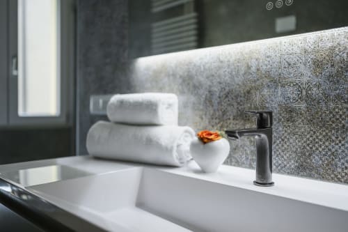 Modern bathroom sink with black faucet, white towels, and decorative flower at Arena Gateway apartment in Verona